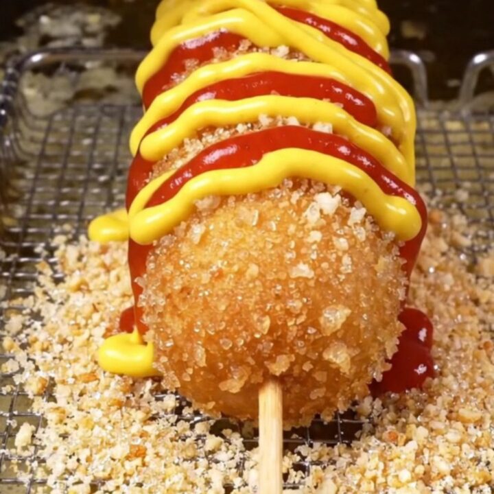 A sugar-dusted Korean corn dog with a long mozzarella pull, showing the crispy panko crust.