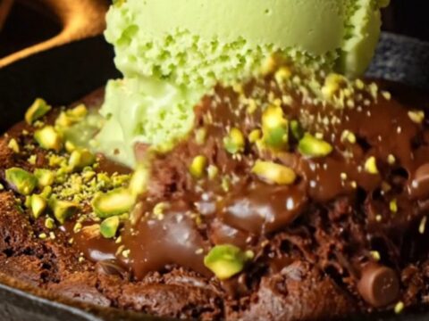 Warm chocolate skillet cookie with pistachio gelato melting on top, showing gooey center and crunchy pistachio pieces