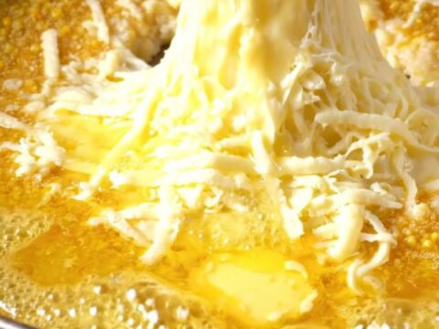 A copper pan of Karadeniz Mıhlama with melted cheese and butter, a piece of bread pulling a long cheese strand.