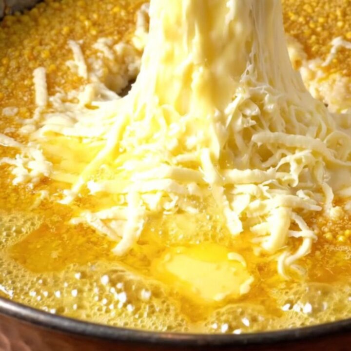 A copper pan of Karadeniz Mıhlama with melted cheese and butter, a piece of bread pulling a long cheese strand.