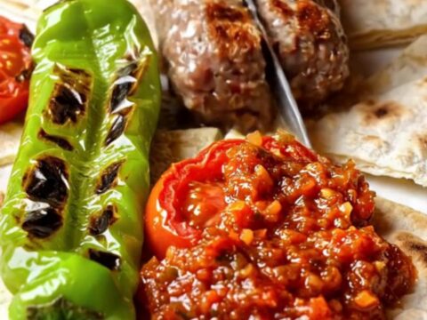 Turkish İnegöl köfte on a grill pan with charred peppers and tomatoes
