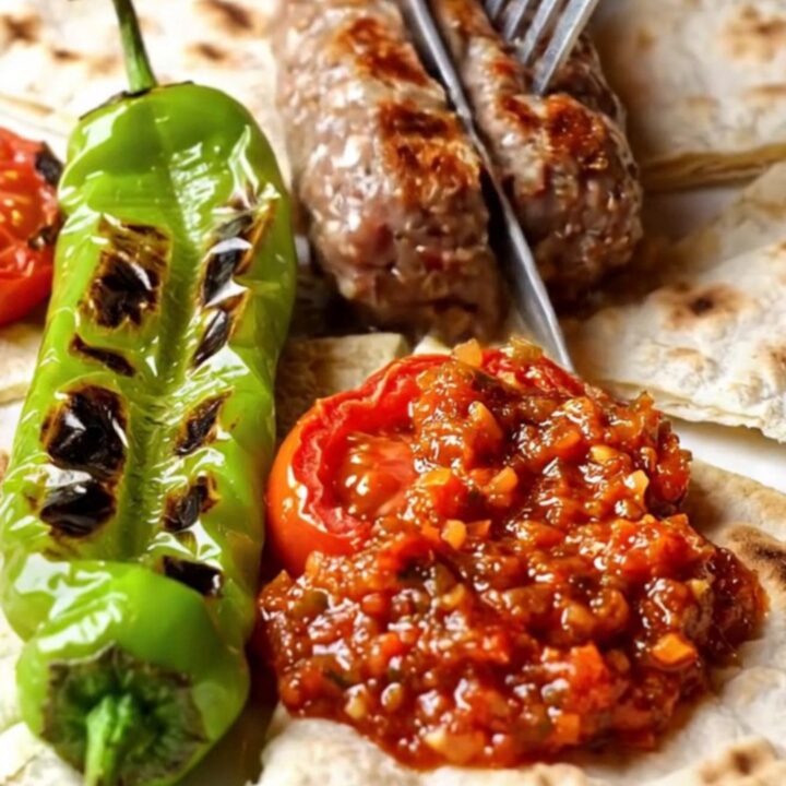 Turkish İnegöl köfte on a grill pan with charred peppers and tomatoes