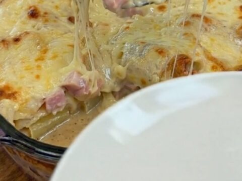 A warm, bubbling baked potato casserole with ham in a glass dish, featuring a massive, gooey mozzarella cheese pull.