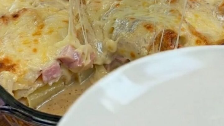A warm, bubbling baked potato casserole with ham in a glass dish, featuring a massive, gooey mozzarella cheese pull.