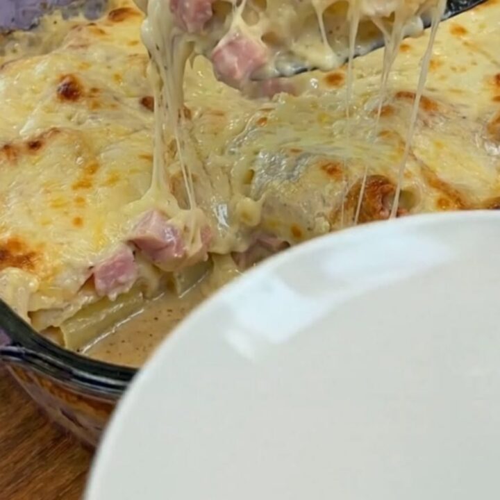 A warm, bubbling baked potato casserole with ham in a glass dish, featuring a massive, gooey mozzarella cheese pull.