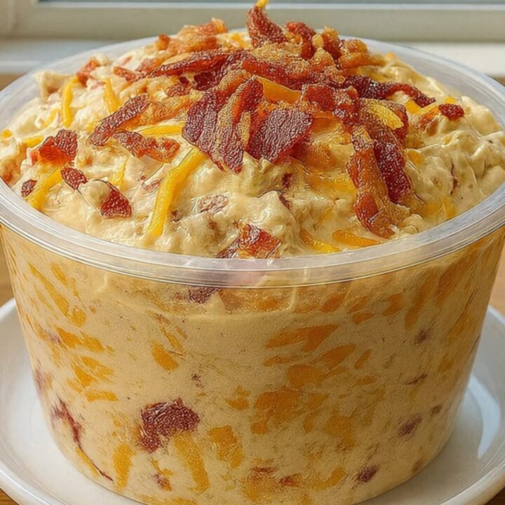 A close-up of a crispy potato chip scooping a large, creamy dollop of cheddar ranch bacon dip from a glass container.