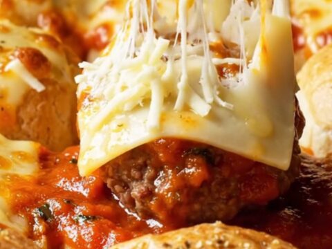 Cheesy garlic-knot meatball sliders in a baking dish with golden brioche tops and melted mozzarella.