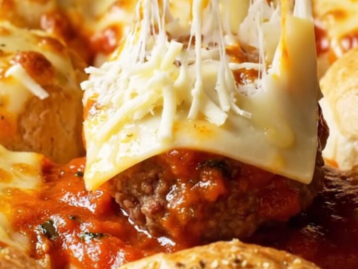 Cheesy garlic-knot meatball sliders in a baking dish with golden brioche tops and melted mozzarella.