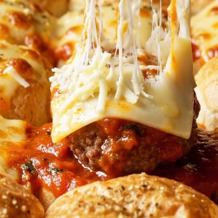 Cheesy garlic-knot meatball sliders in a baking dish with golden brioche tops and melted mozzarella.