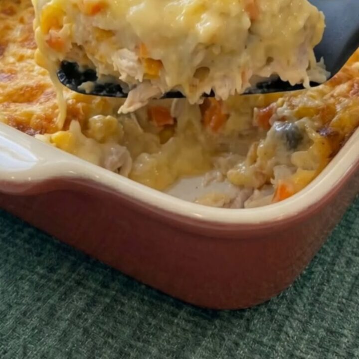Cuillère soulevant une portion de chicken cobbler crémeux avec du fromage filant et une croûte dorée.