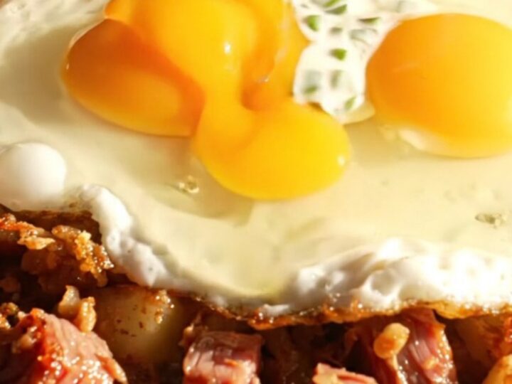 Crispy corned beef hash with two fried eggs and horseradish chive crema in a cast-iron skillet
