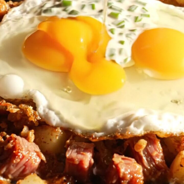 Crispy corned beef hash with two fried eggs and horseradish chive crema in a cast-iron skillet