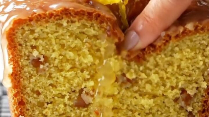 Golden glazed whole-lemon blender cake on a wooden board, sliced to show moist yellow crumb with walnuts