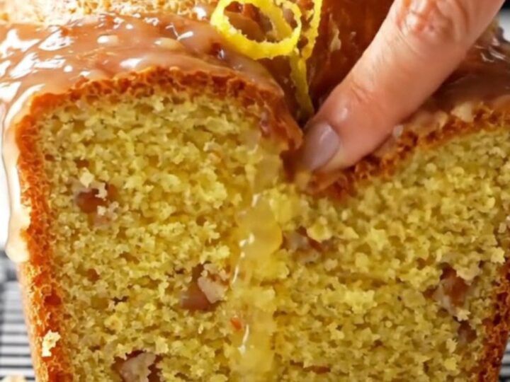 Golden glazed whole-lemon blender cake on a wooden board, sliced to show moist yellow crumb with walnuts