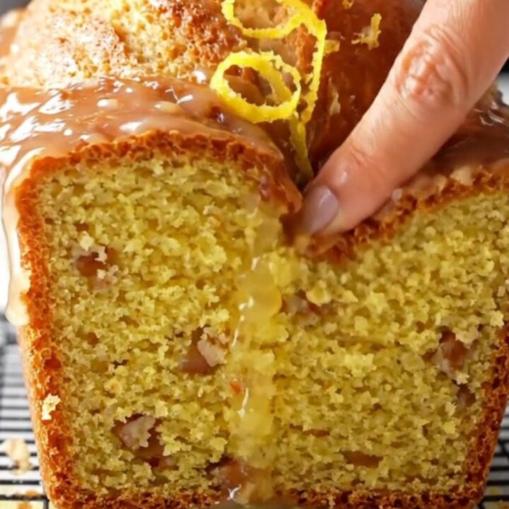 Golden glazed whole-lemon blender cake on a wooden board, sliced to show moist yellow crumb with walnuts