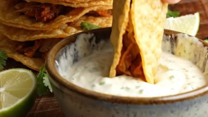 Crispy chipotle chicken mini tacos stacked on a wooden board with lime crema dip