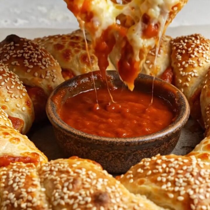 Golden crown pizza with braided crust, sesame seeds, and a bowl of marinara in the center