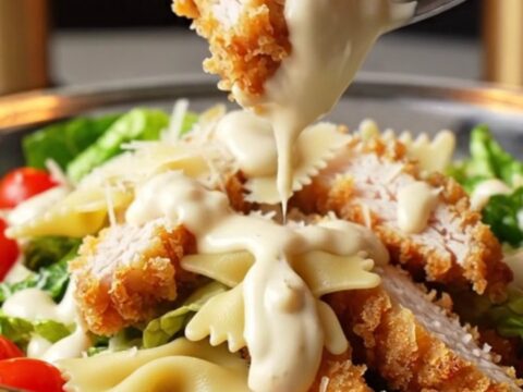 Crispy chicken Caesar pasta salad in a large bowl, with golden chicken strips, bowtie pasta, romaine, and cherry tomatoes.