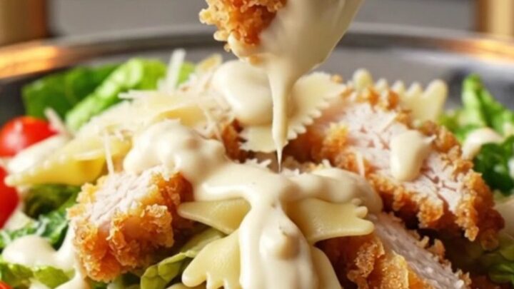 Crispy chicken Caesar pasta salad in a large bowl, with golden chicken strips, bowtie pasta, romaine, and cherry tomatoes.