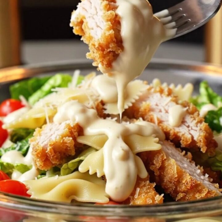 Crispy chicken Caesar pasta salad in a large bowl, with golden chicken strips, bowtie pasta, romaine, and cherry tomatoes.
