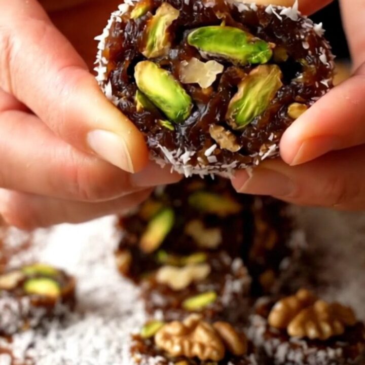 A slicing knife cutting a coconut-coated date roll, revealing green pistachios and walnut halves inside.