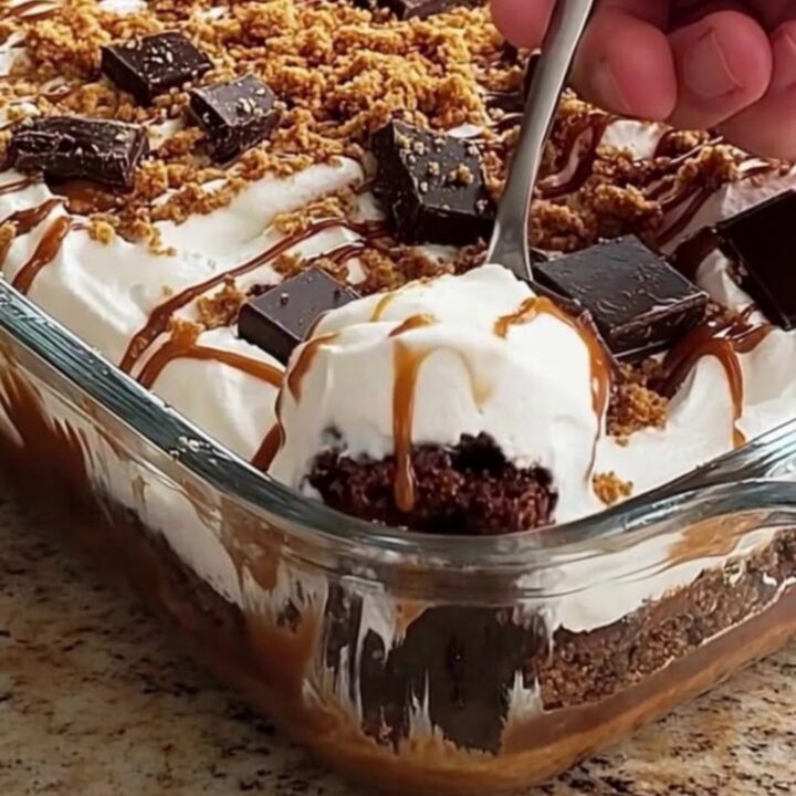 A clear glass casserole dish filled with layers of chocolate cake, whipped cream, and caramel