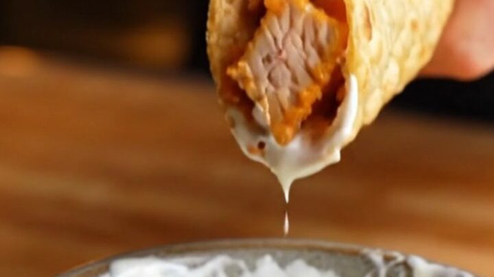 Crispy folded chipotle chicken taco lifted from a sheet pan, with melted cheese stretching