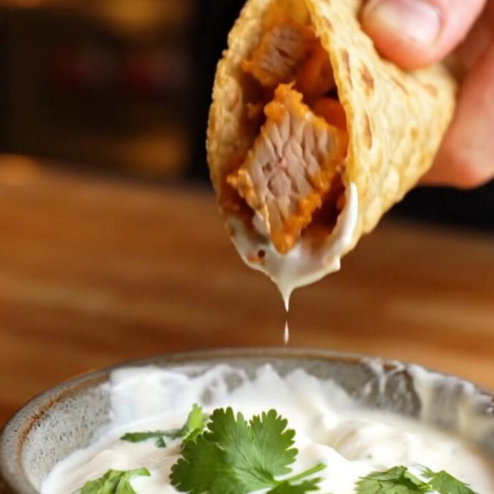 Crispy folded chipotle chicken taco lifted from a sheet pan, with melted cheese stretching