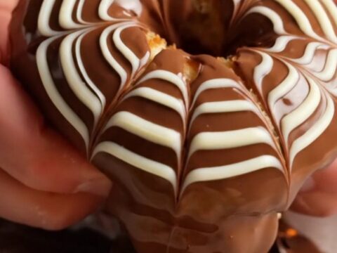 Fluffy chocolate-glazed ring donuts with white chocolate feather design on a wire rack