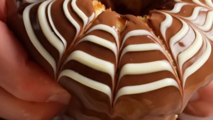 Fluffy chocolate-glazed ring donuts with white chocolate feather design on a wire rack