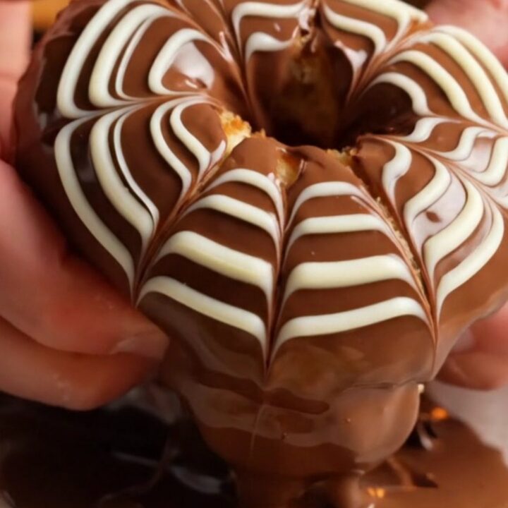 Fluffy chocolate-glazed ring donuts with white chocolate feather design on a wire rack