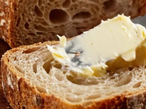 A dark golden artisan sourdough loaf with a blistered crust and a prominent ear, sliced to show an airy, honeycomb crumb.