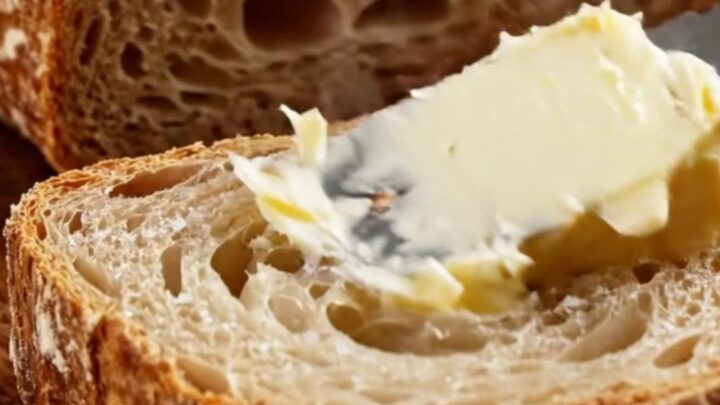 A dark golden artisan sourdough loaf with a blistered crust and a prominent ear, sliced to show an airy, honeycomb crumb.