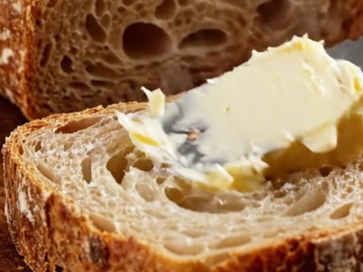 A dark golden artisan sourdough loaf with a blistered crust and a prominent ear, sliced to show an airy, honeycomb crumb.