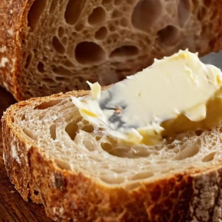 A dark golden artisan sourdough loaf with a blistered crust and a prominent ear, sliced to show an airy, honeycomb crumb.