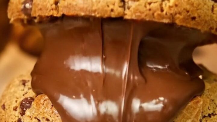 Giant cookie broken open showing molten hazelnut cream and chopped Kinder Bueno pieces on parchment paper