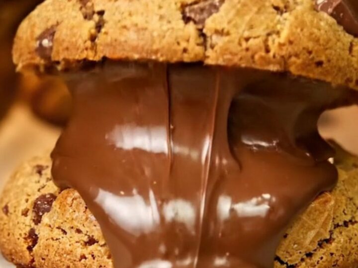 Giant cookie broken open showing molten hazelnut cream and chopped Kinder Bueno pieces on parchment paper