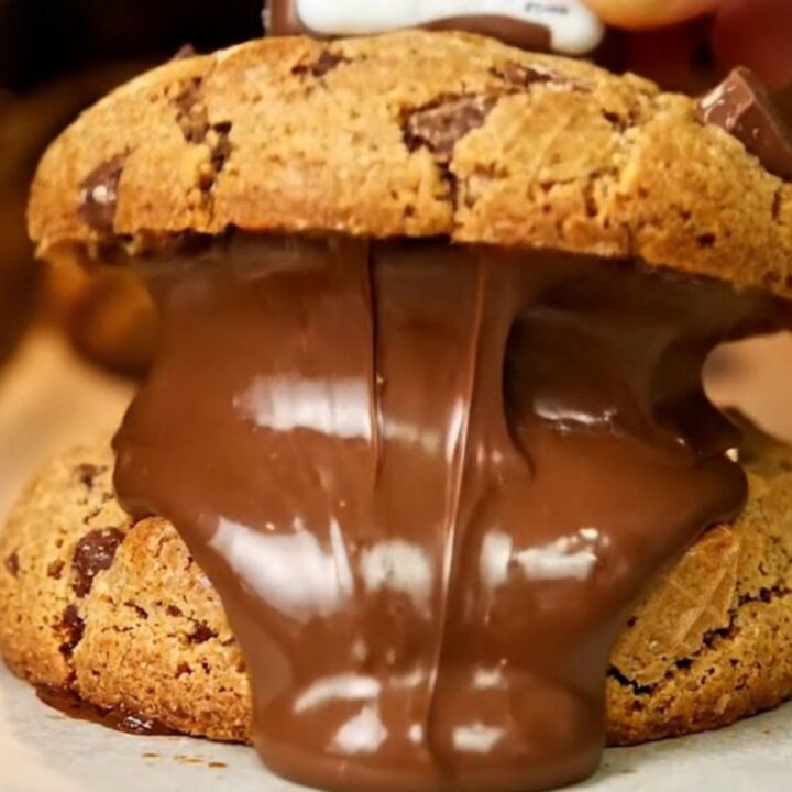 Giant cookie broken open showing molten hazelnut cream and chopped Kinder Bueno pieces on parchment paper