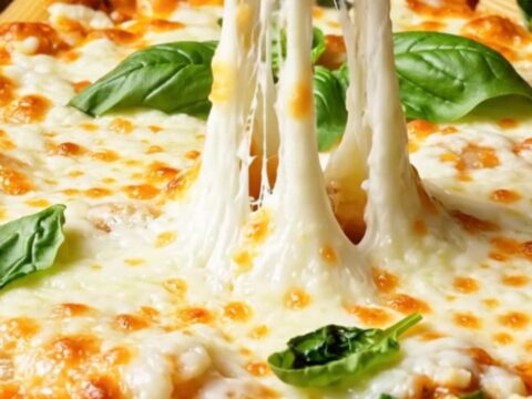 Spoon scooping creamy rigatoni with melted mozzarella pulling in long threads