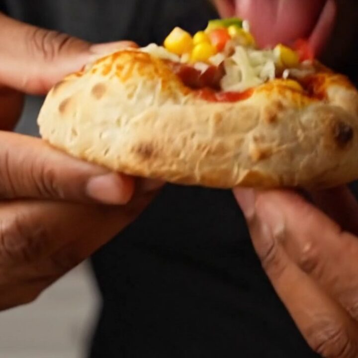 Fluffy golden mini pizzas with melted mozzarella, sucuk slices, peppers, and corn on a parchment-lined baking sheet.