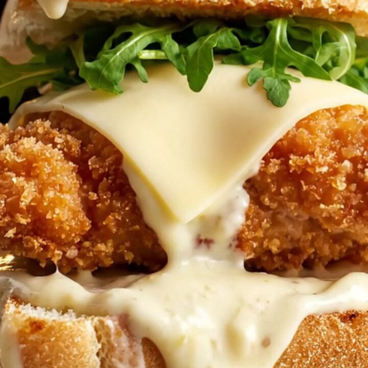 A crispy chicken Alfredo sandwich on toasted garlic ciabatta, cut in half showing melted provolone and arugula.