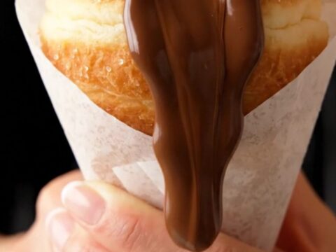 A sugar-coated donut in a paper cone, oozing chocolate hazelnut spread