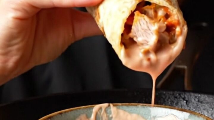 A diagonal slice of a toasted chicken wrap showing juicy spiced chicken, crunchy salad, and pink yogurt sauce.