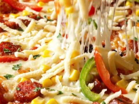 Golden sheet pan crepe pizza with melted cheese, sucuk, corn, and peppers, cut into squares