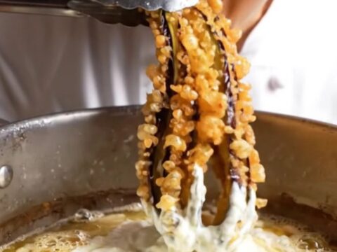 Whole fried eggplant blooming like an octopus, golden and crispy, on a white plate with a bowl of garlic yogurt.