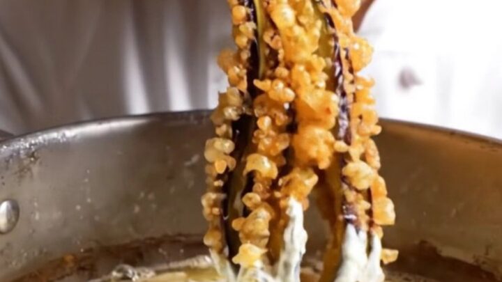 Whole fried eggplant blooming like an octopus, golden and crispy, on a white plate with a bowl of garlic yogurt.