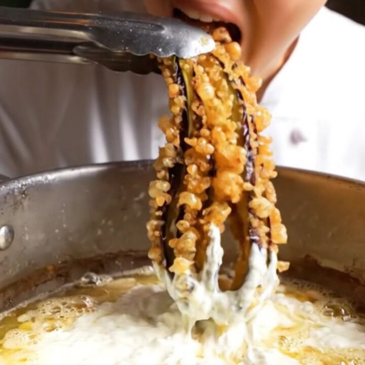 Whole fried eggplant blooming like an octopus, golden and crispy, on a white plate with a bowl of garlic yogurt.
