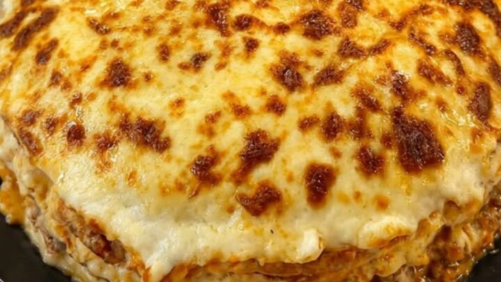 A slice of cheesy crepe lasagna on a black plate showing distinct layers of meat sauce and crepe.