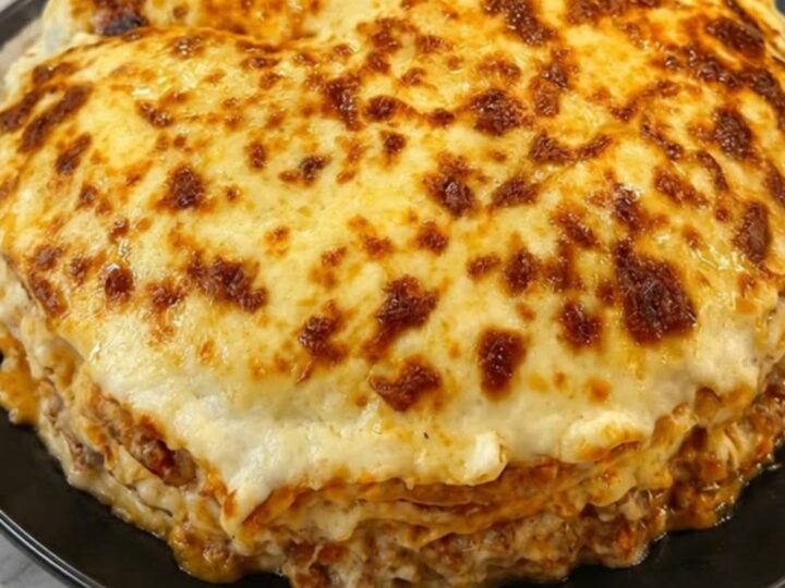A slice of cheesy crepe lasagna on a black plate showing distinct layers of meat sauce and crepe.