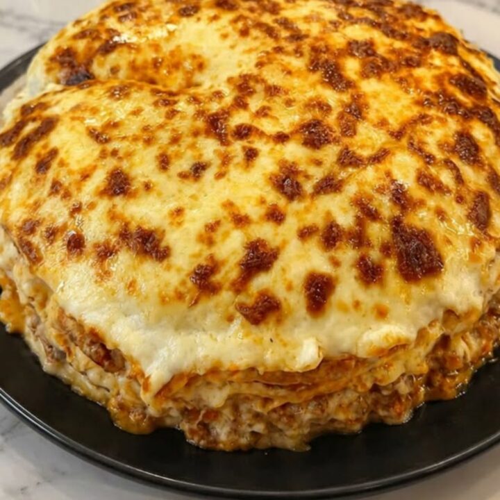 A slice of cheesy crepe lasagna on a black plate showing distinct layers of meat sauce and crepe.